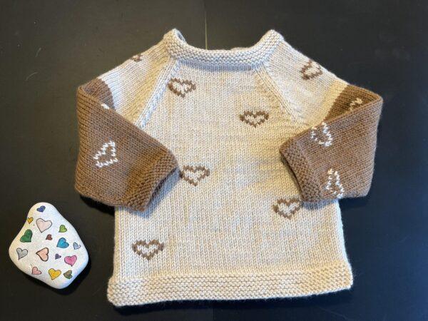 Opskrift på Strikket babybluse til baby med hjerter mønster og farvede hjerter, sten dekoreret med farverige hjerter på sort baggrund