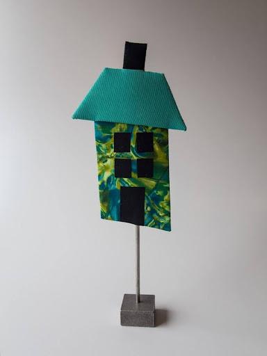 Patchwork stof​. Farverig miniaturemodel af et hus med blåt tag, abstrakt mønster på væggene og sort dør på en metalstand.