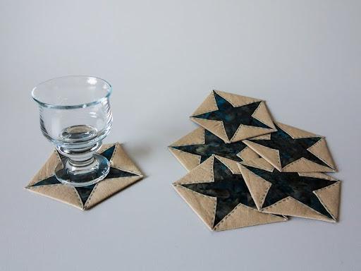 Glas står på kaffebrik med stjernemønster ved siden af flere lignende dækkeservietter på hvid baggrund.