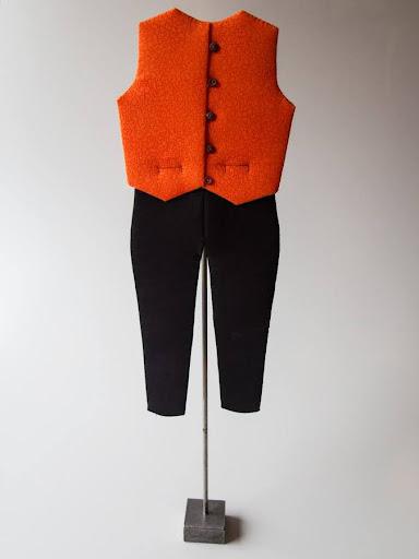 Patchwork - Orange uldvest og sorte bukser på en mannequin-stang, set bagfra.