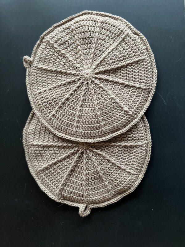 Crochet potholders in a patterned design, beige color on a black background. Oval shape and decorative details.