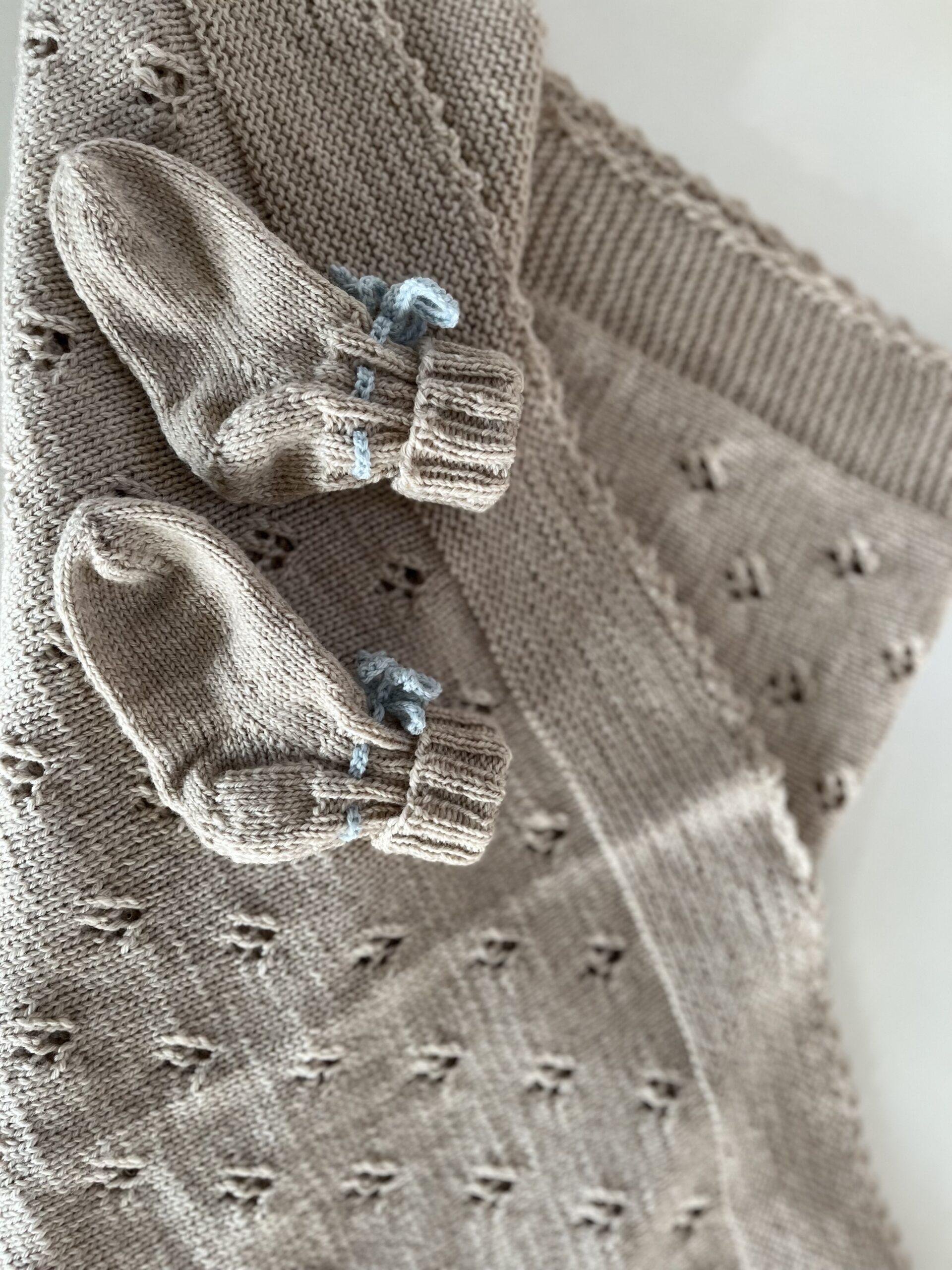 Beige strikkede sokker med lyseblå detaljer, placeret på en baggrund af tekstureret stof.