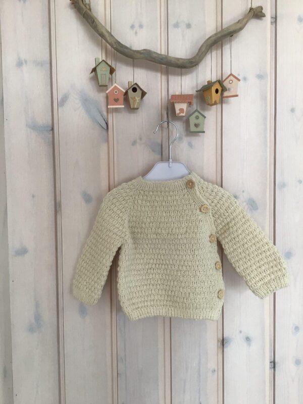 Håndstrikket baby sweater på bøjle, med fuglehuse som dekoration i baggrunden.
