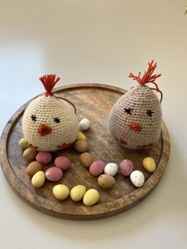 Crocheted Easter chickens and colorful chocolate eggs on a round wooden platter, ready for spring decoration.
