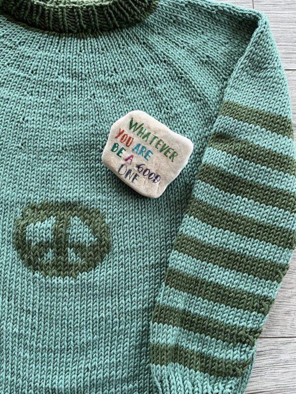 Knitted sweater for kids. A green sweater featuring a peace sign and a button that reads, "Waiting for the Beat to Drop."