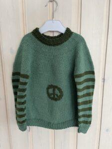Green knitted sweater with dark green stripes and peace sign hangs on wooden background.