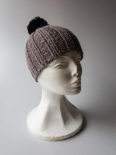 Pelskvast til hue - Strikket hue i beige med sort kvast vist på hvid mannequin hoved mod neutral baggrund.