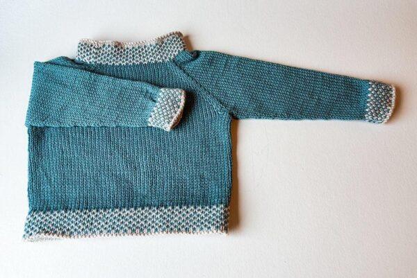 Blåstrikket sweater til børn med mønster ved manchetter og hals på lysegrå baggrund. Perfekt til kølige dage.