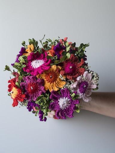 Hæklet buket. Buketter af hæklede blomster i levende farver holdes i hånd mod en grå baggrund.