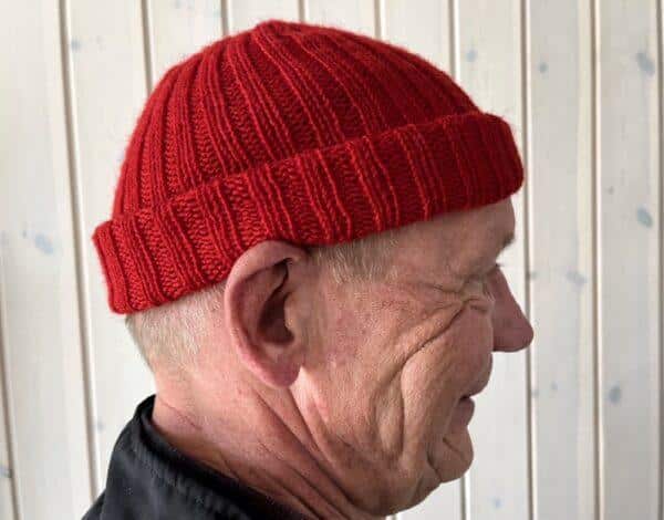 Mand iført rødstrikket hipster hue set fra siden, foran en lys trævæg.