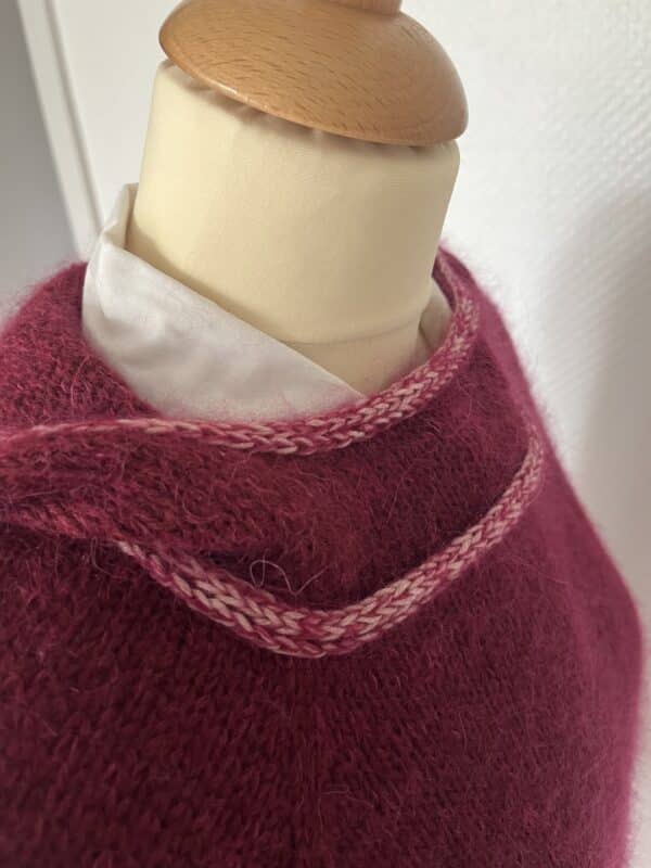A close-up of a maroon knitted sweater hoodie on a mannequin with a white collared shirt underneath and a decorative neckline.