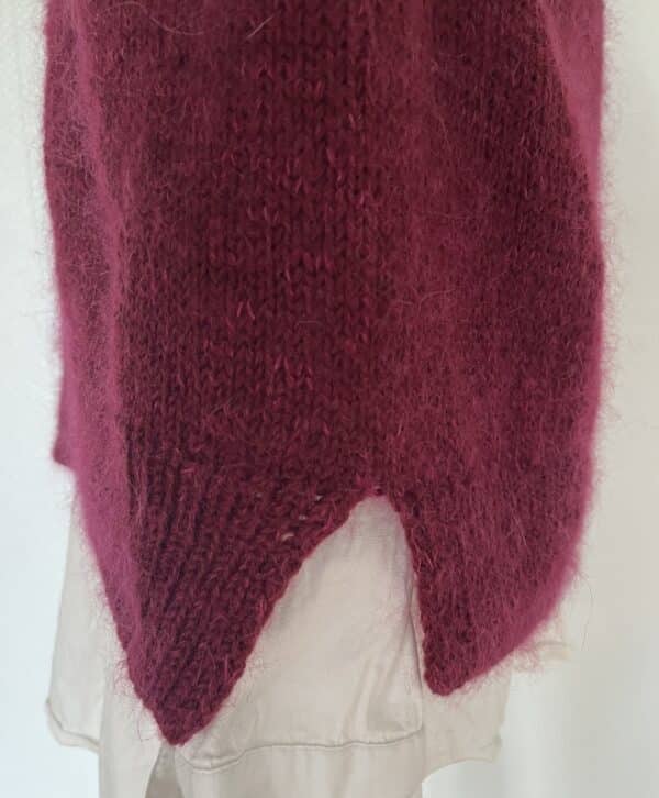 Close-up of a maroon, soft knit sweater hoodie with a V-shaped hem, layered over a light shirt.