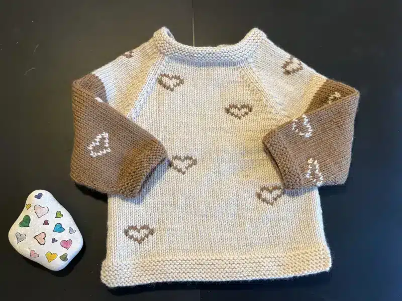 Strikket bluse. Strikket bluse. En hyggelig beige sweater med brune ærmer og hjertemønstre, parret med en farverig hjertedekoreret sten.